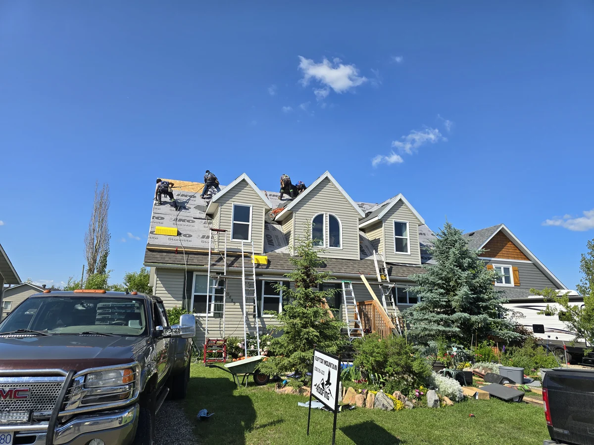 Roofing crew working on the gabled roof of a two-storey house with ladders in place
