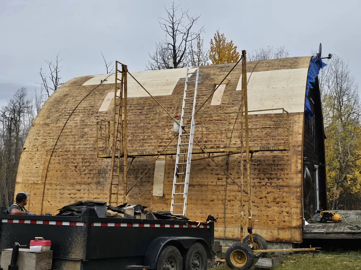 Steep roof with shingles removed, exposed wood decking, scaffold and ladder