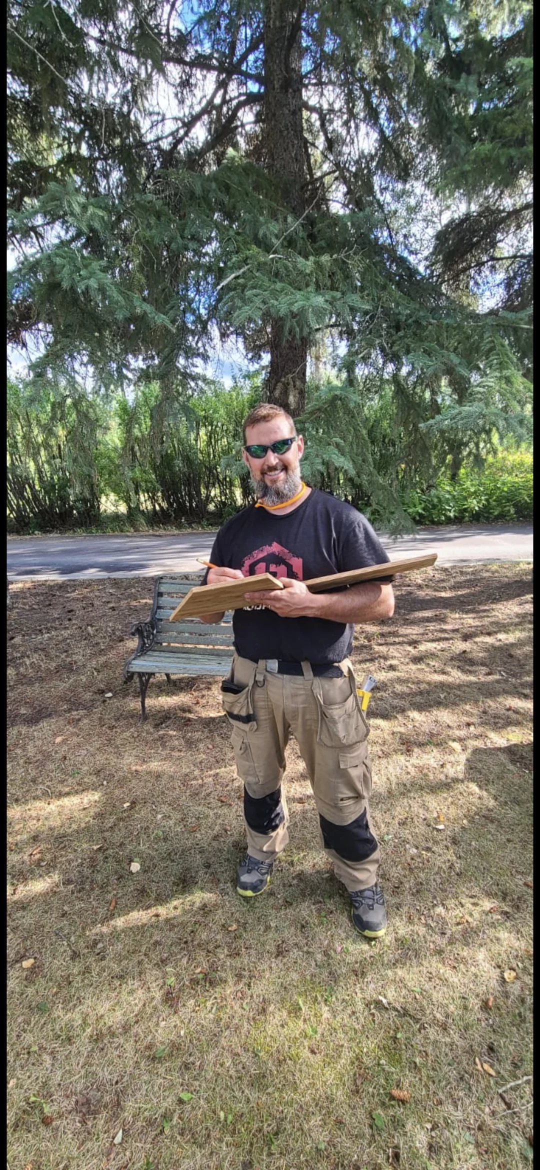 Man holding a clipboard outdoors beside trees