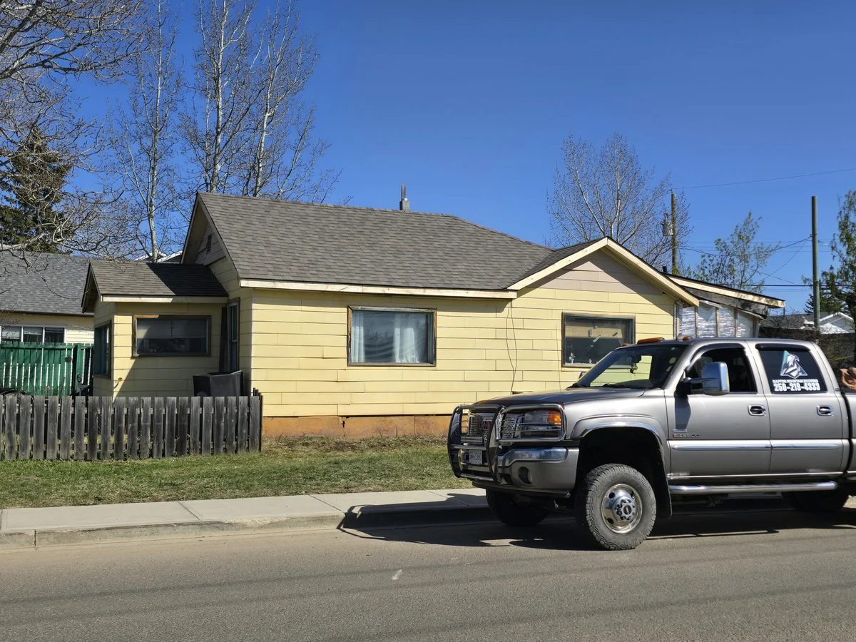 Shingle roof on a yellow house with a pickup truck in front